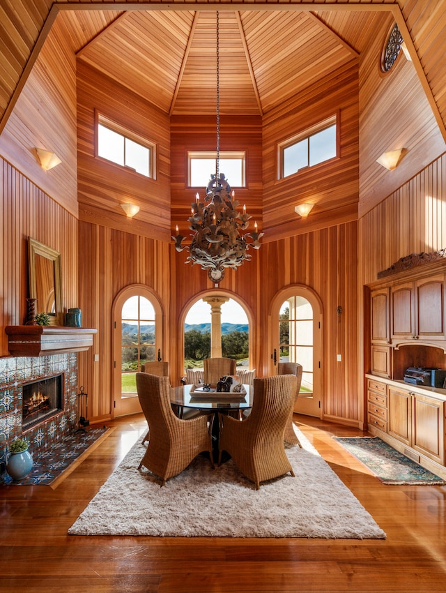 interior space with a tile fireplace, high vaulted ceiling, wood ceiling, wooden walls, and an inviting chandelier