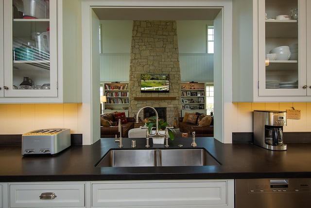 kitchen with sink, white cabinetry, dishwasher, and a stone fireplace