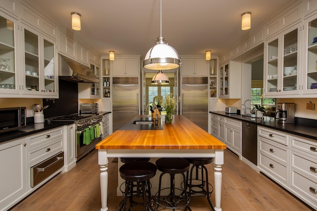 kitchen with high quality appliances, pendant lighting, butcher block counters, and wall chimney exhaust hood