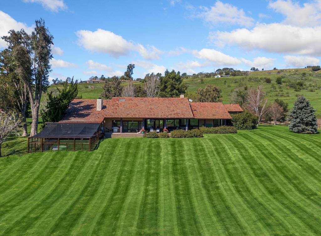 back of property with glass enclosure, a lawn, a chimney, and a tile roof