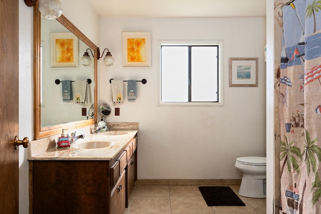 bathroom with baseboards, double vanity, toilet, a sink, and tile patterned flooring