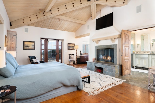 bedroom with a tiled fireplace, high vaulted ceiling, ensuite bath, and beamed ceiling