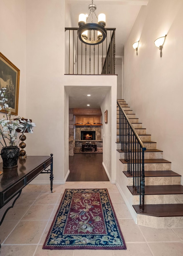 tiled entrance foyer featuring an inviting chandelier, a stone fireplace, and a high ceiling