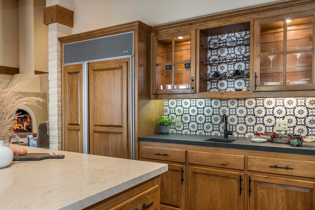 kitchen with backsplash, light stone countertops, sink, and paneled built in refrigerator