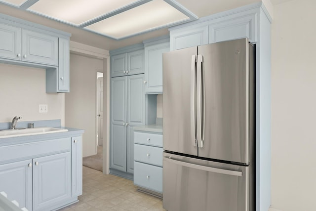 kitchen with light tile floors, stainless steel refrigerator, white cabinetry, and sink