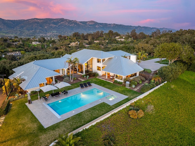 pool at dusk with a mountain view, a patio, and a lawn