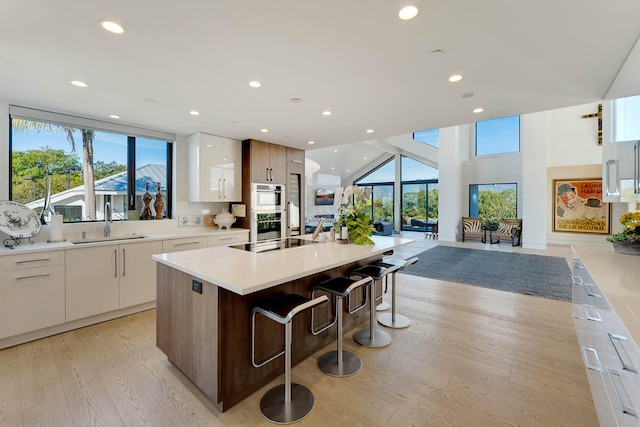 kitchen with a kitchen bar, sink, white cabinetry, an island with sink, and black electric stovetop