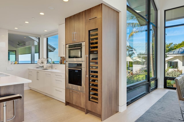 kitchen featuring stainless steel double oven, sink, a healthy amount of sunlight, and white cabinets