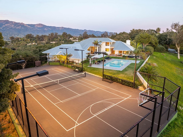 view of tennis court featuring a fenced in pool, a yard, a mountain view, and basketball hoop