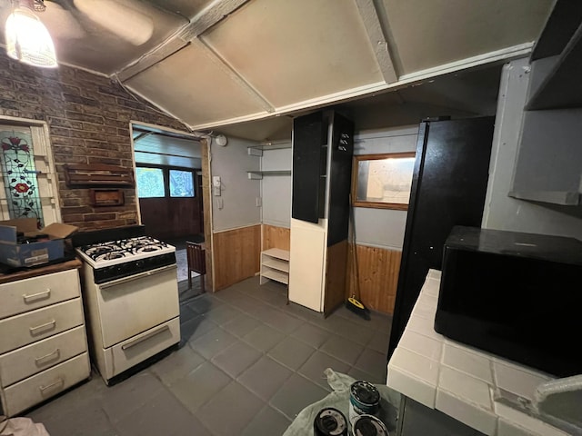 kitchen featuring lofted ceiling, tile floors, white gas stove, and brick wall