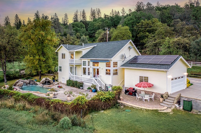 back house at dusk featuring a patio, a yard, a garage, solar panels, and pool water feature