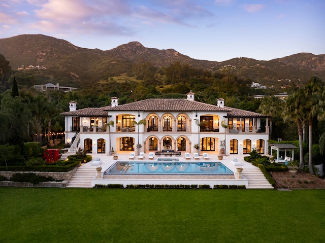 back house at dusk featuring a patio, a yard, and a mountain view