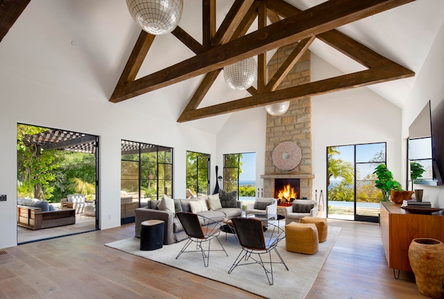 living room featuring high vaulted ceiling, light hardwood / wood-style flooring, beamed ceiling, and a stone fireplace