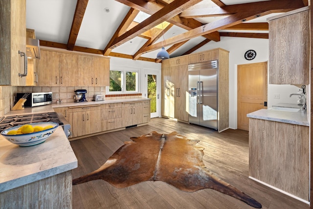 kitchen featuring hardwood / wood-style floors, tasteful backsplash, stainless steel appliances, vaulted ceiling with beams, and sink