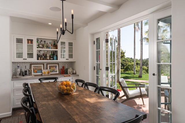 dining space featuring beam ceiling, a chandelier, bar area, and hardwood / wood-style floors