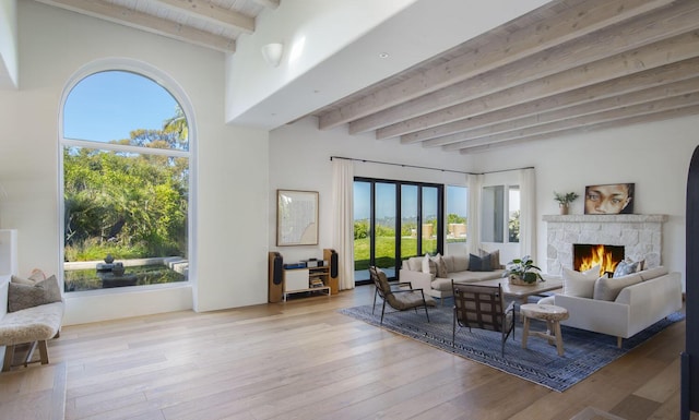 living area featuring beam ceiling, a stone fireplace, and hardwood / wood-style flooring