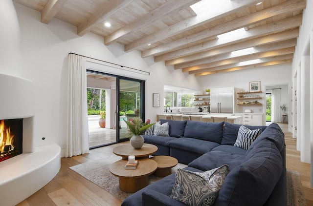 living area with beam ceiling, recessed lighting, wood ceiling, light wood-type flooring, and a warm lit fireplace