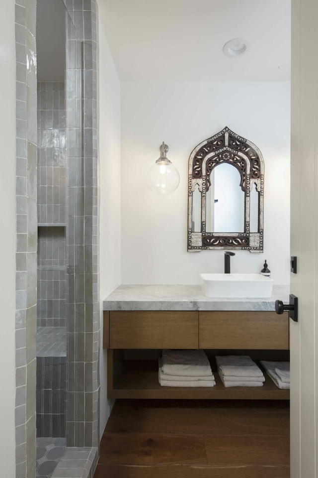 bathroom with a tile shower, wood finished floors, and vanity