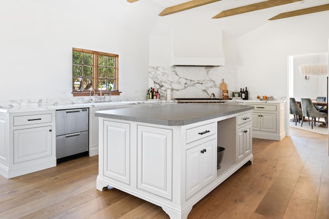 kitchen with a kitchen island, beamed ceiling, decorative backsplash, white cabinets, and light wood-type flooring