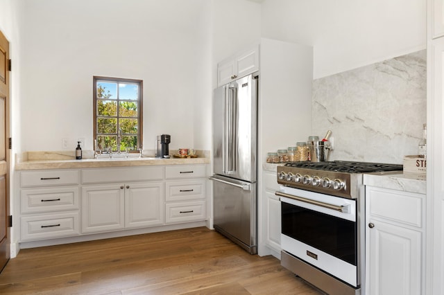 kitchen featuring high end appliances, white cabinetry, sink, and light wood-type flooring