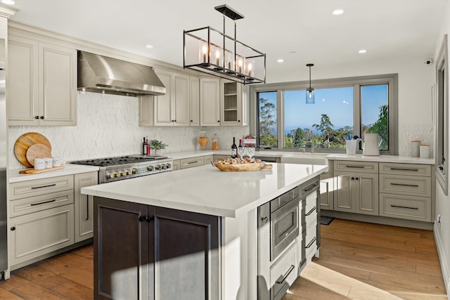 kitchen with stainless steel appliances, a center island, light hardwood / wood-style floors, and wall chimney range hood