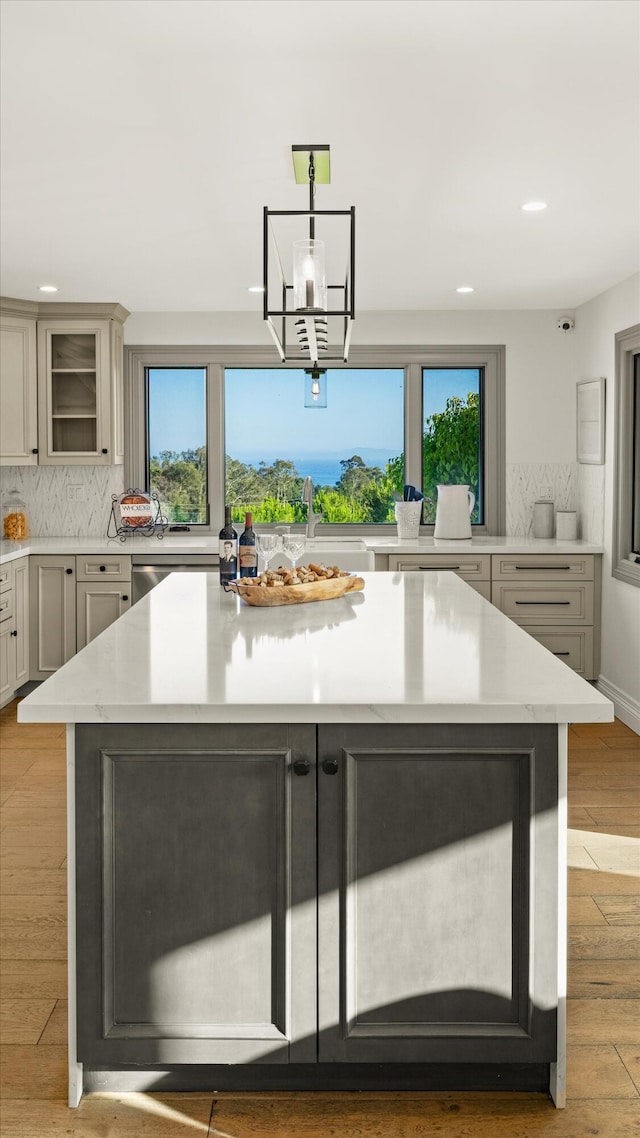 kitchen featuring pendant lighting, sink, gray cabinetry, backsplash, and light wood-type flooring