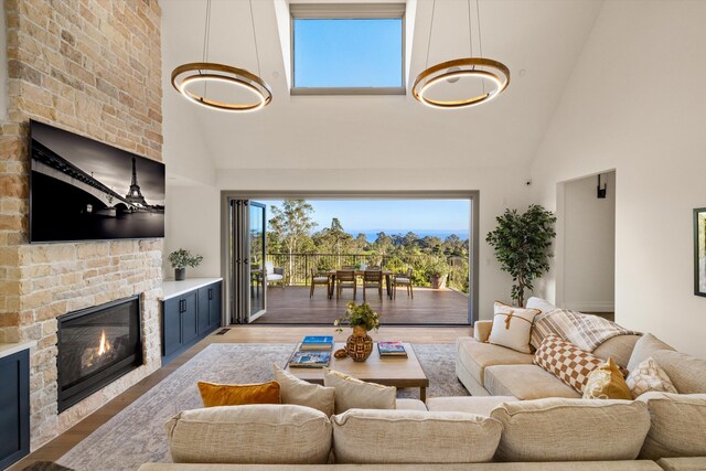 living room with a stone fireplace, light wood-type flooring, and high vaulted ceiling