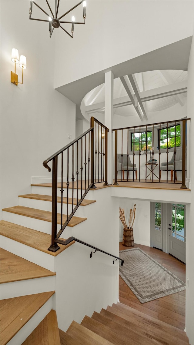 stairs with beam ceiling, a towering ceiling, wood-type flooring, and a healthy amount of sunlight