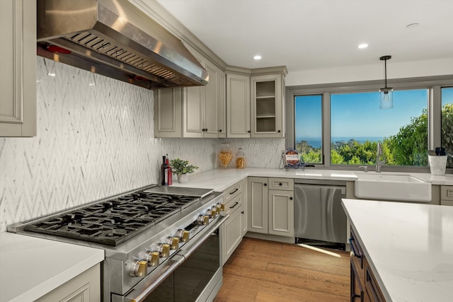 kitchen featuring pendant lighting, sink, wall chimney exhaust hood, stainless steel appliances, and light hardwood / wood-style flooring