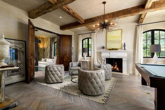 living area with beam ceiling, a notable chandelier, a lit fireplace, and baseboards