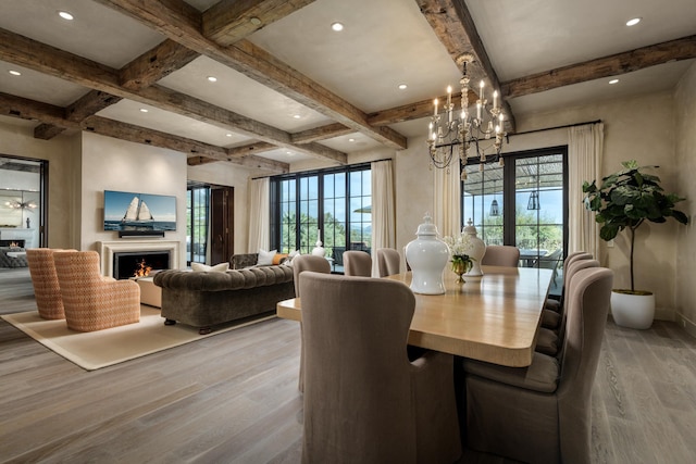 dining space featuring a notable chandelier, a warm lit fireplace, light wood-style flooring, and beam ceiling