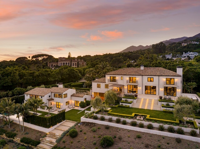 back of property at dusk featuring a fenced front yard, a mountain view, a chimney, and stucco siding