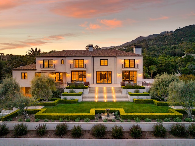 back house at dusk with a mountain view and a yard