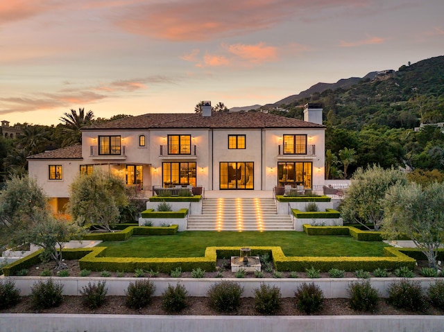 back of property at dusk with a yard, a mountain view, and stucco siding