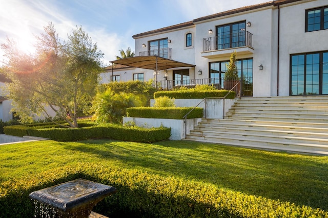 back of house featuring stairs, a lawn, and stucco siding