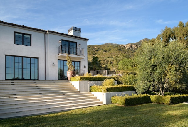 back of house featuring a chimney, stucco siding, a lawn, stairway, and a mountain view