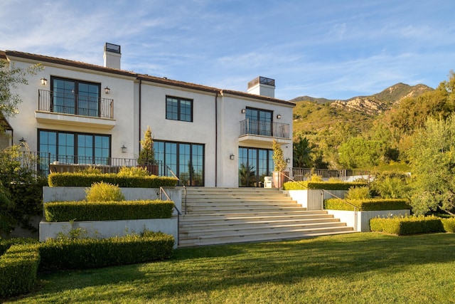 rear view of property featuring a chimney, stairs, a yard, a mountain view, and stucco siding