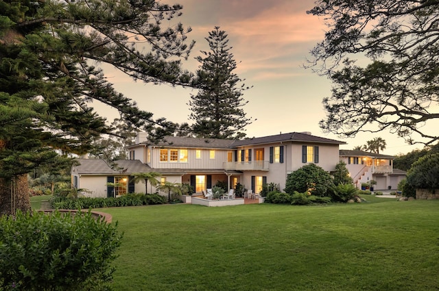 back house at dusk with a balcony and a yard