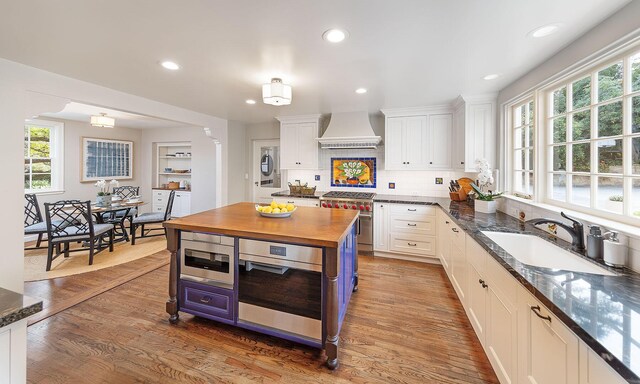 kitchen with sink, wooden counters, white cabinetry, stainless steel appliances, and custom range hood