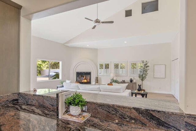living area featuring high vaulted ceiling, a glass covered fireplace, visible vents, and ceiling fan