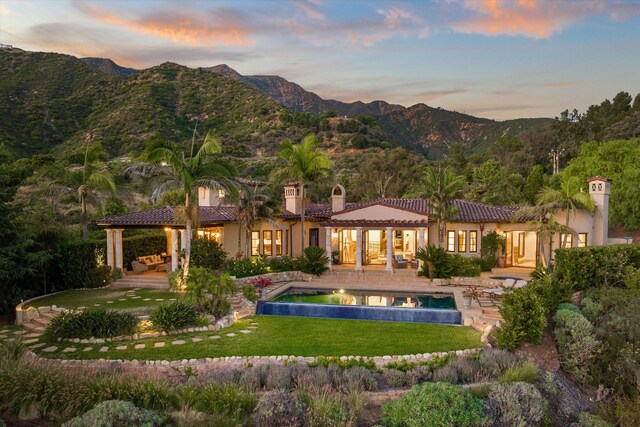 back house at dusk featuring a lawn, a mountain view, outdoor lounge area, and a patio