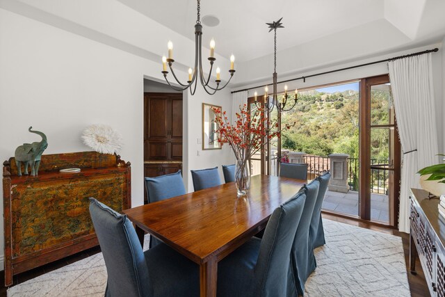 dining space featuring a raised ceiling, an inviting chandelier, and light wood-type flooring