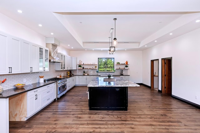 kitchen with a tray ceiling, wall chimney range hood, decorative light fixtures, double oven range, and white cabinets