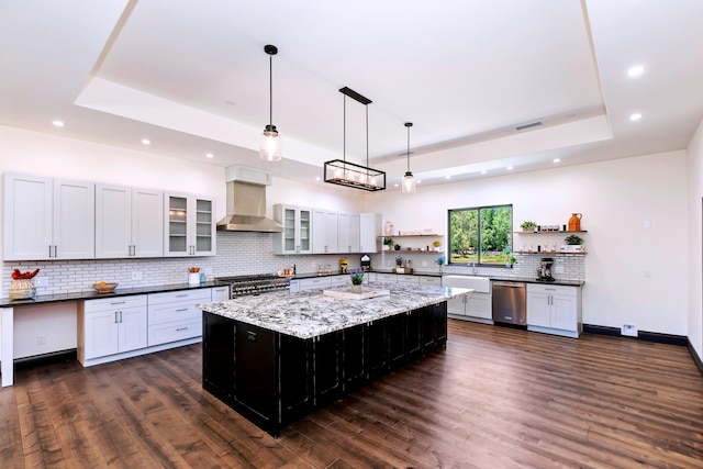 kitchen with a large island, hanging light fixtures, wall chimney range hood, stainless steel appliances, and a raised ceiling