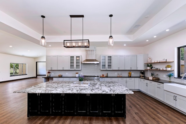 kitchen with pendant lighting, a spacious island, wall chimney range hood, and range