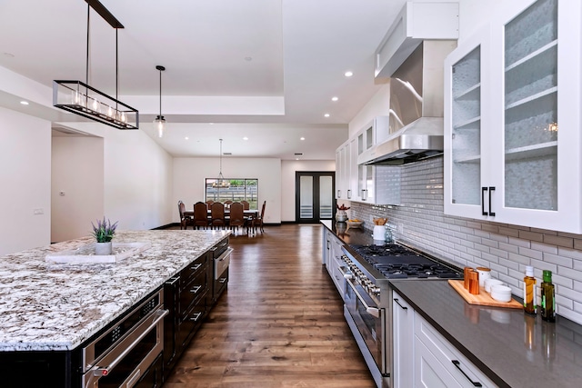 kitchen with backsplash, white cabinets, hanging light fixtures, wall chimney exhaust hood, and appliances with stainless steel finishes