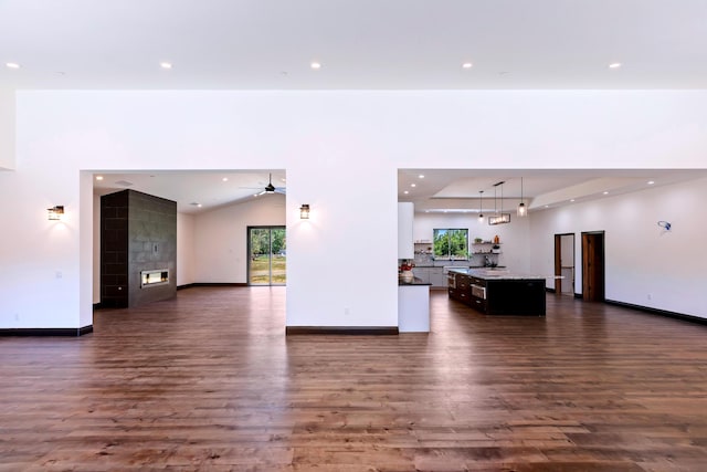 unfurnished living room featuring dark hardwood / wood-style flooring, ceiling fan, and a tiled fireplace