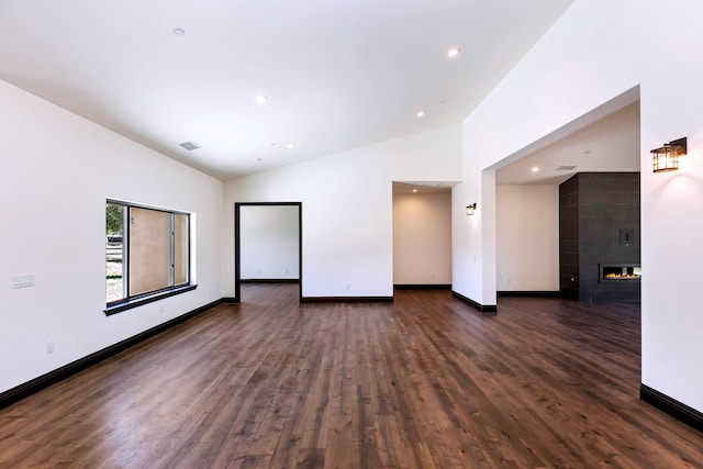 spare room featuring dark wood-type flooring, high vaulted ceiling, and a tiled fireplace