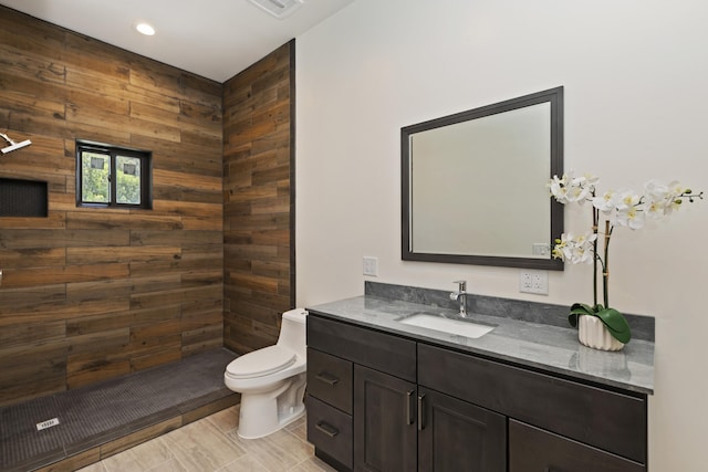 bathroom featuring vanity, wood walls, tile patterned floors, toilet, and tiled shower