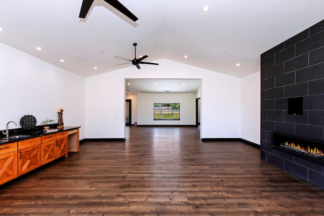 living room with ceiling fan, sink, dark hardwood / wood-style flooring, vaulted ceiling, and a fireplace